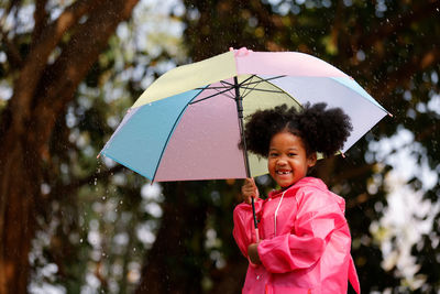 Portrait of happy woman holding pink umbrella during rainy season