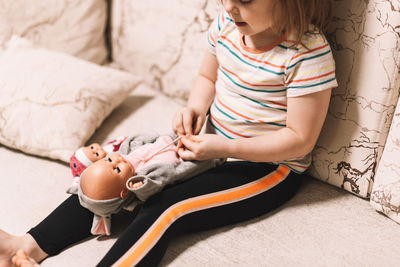 Child learns to tie shoelaces at home by playing with a doll. 