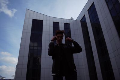 Full length portrait of young man standing against modern office building