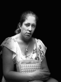 Portrait of young woman sitting against black background