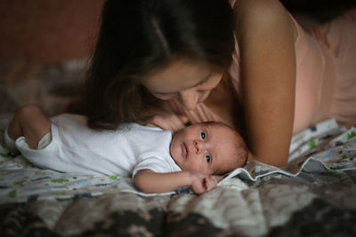 Close-up of cute baby boy lying on bed at home and kissing mom