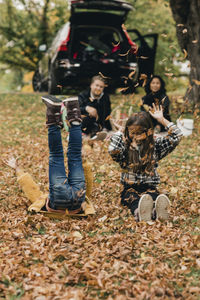 Playful sisters enjoying on autumn leaves during picnic with parents