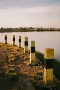 Wooden posts on field by lake against sky