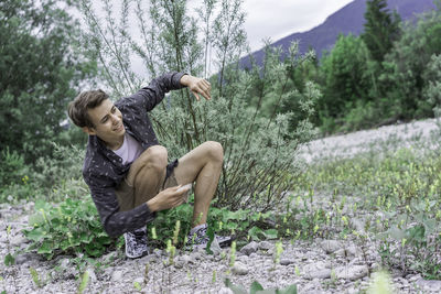 Happy man crouching by plant in forest