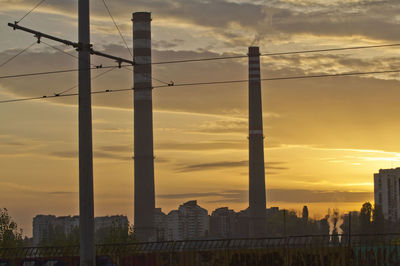 Electricity pylon and buildings against sky during sunset