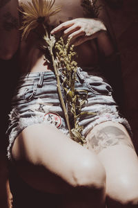 Midsection of shirtless woman with flowers in sunlight