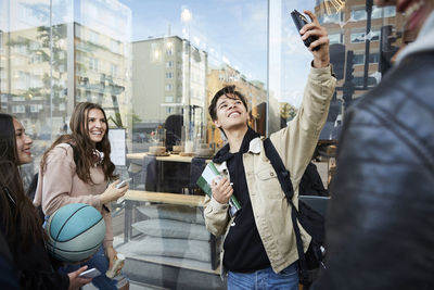 Smiling friends taking selfie while standing in city