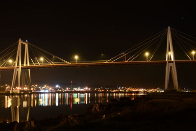 Illuminated bridge over river against sky at night