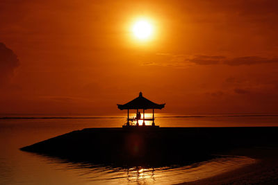 Silhouette lifeguard hut on beach against sky during sunset