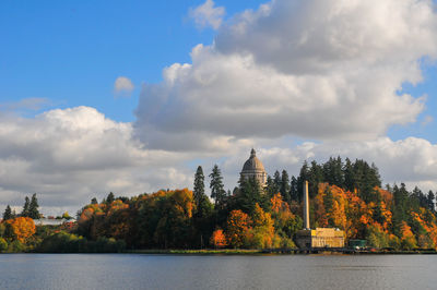 Scenic view of river by trees and buildings against sky