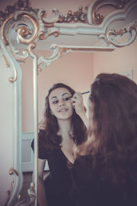 Young woman applying eyeliner while looking in mirror