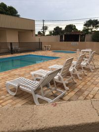 Empty chairs and tables by swimming pool against sky