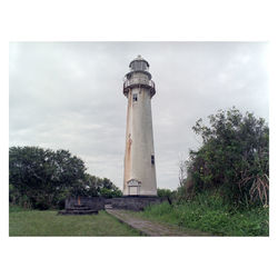 Lighthouse amidst trees and buildings against sky