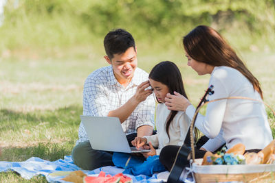 Happy father and mother looking at daughter using laptop at park