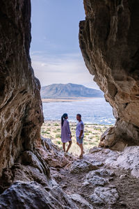 People looking at sea by rock formation against sky