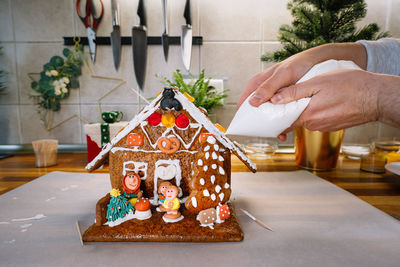 Midsection of person decorating christmas gingerbread house in kitchen at home