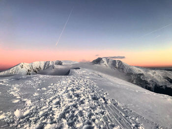 Snow covered landscape against sky during sunset