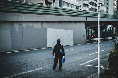 Rear view of woman standing on road by bridge