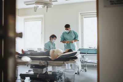 Male and female surgeons examining patient on bed in hospital