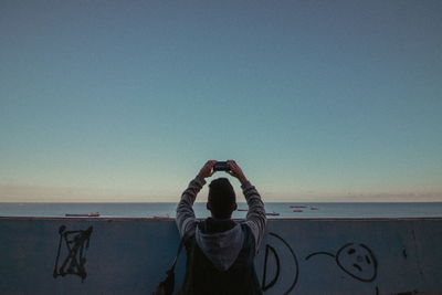 Rear view of man photographing through mobile phone at beach against sky