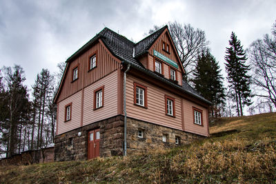 Low angle view of cottage amidst trees and building against sky