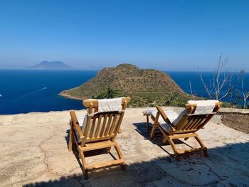 Deck chairs on beach against sky