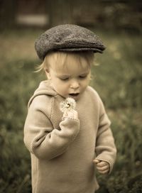 High angle view of boy holding dandelion seed while standing on grassy field at park