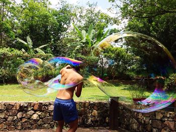 Rear view of boy playing with large bubble in park