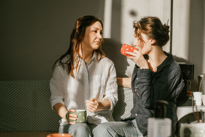 Two female friends enjoying morning coffee in cozy home kitchen