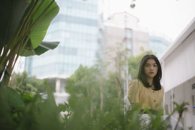 Portrait of young woman standing by plants in city