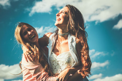 Low angle view of smiling friends standing against cloudy sky