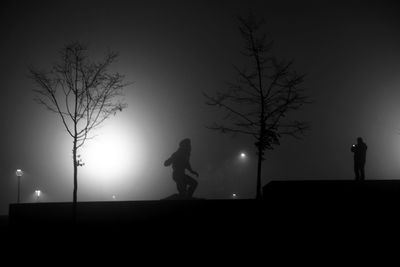 Silhouette man standing by illuminated tree against sky at night