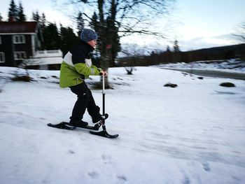 Side view full length of boy riding push scooter on snow covered field