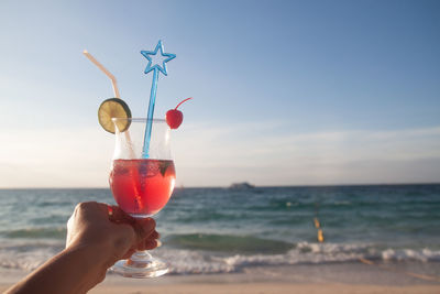 Midsection of person holding drink at beach against sky