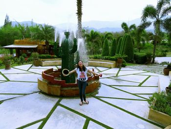 Cheerful young woman enjoying by fountain at park