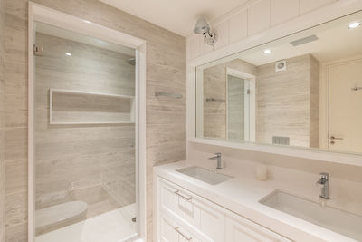 Interior of  bathroom with beige tiles, transparent door to the shower and sinks in refurbished flat