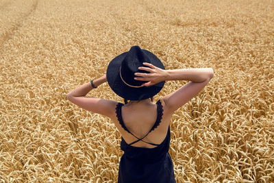 Woman in a black dress and a hat stands in a yellow field