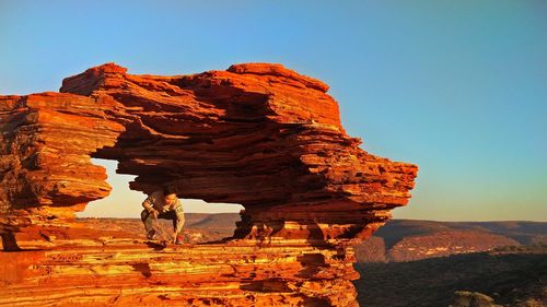 Man crouching in rock formation at desert during sunset