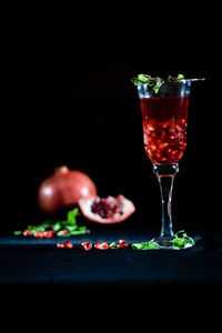 Pomegranate juice in glass on table against black background