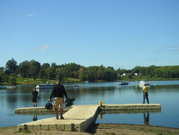 Rear view of men sitting on riverbank against clear sky