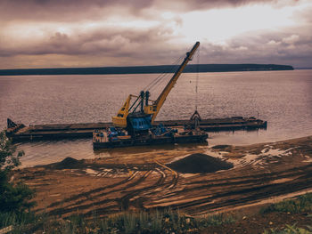 Construction site by sea against sky during sunset