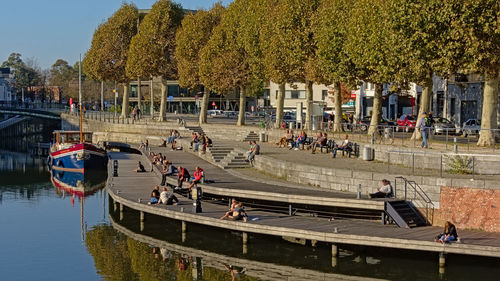 People by boats in river against trees