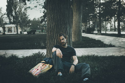 Portrait of young man sitting on plant against trees