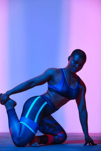 Side view of woman exercising against colored background