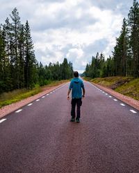 Rear view of man walking on road against sky