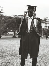 Man wearing graduation gown and mortarboard while standing at campus