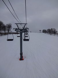 Ski lift on snow covered field against sky