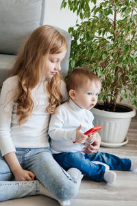 Girl with a baby brother sitting on the floor with a smartphone