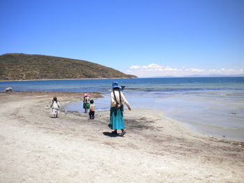 Rear view of mother walking with children on shore at beach
