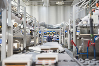 Two men talking at conveyor belt in factory shop floor